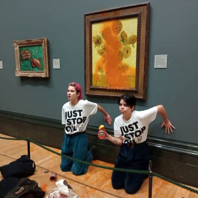 Två aktivister i matchande Just Stop Oil-t-tröjor har limmat var sin hand mot väggen nedanför van Goghs målning Solrosor, som rinner av orangefärgad tomatsoppa.