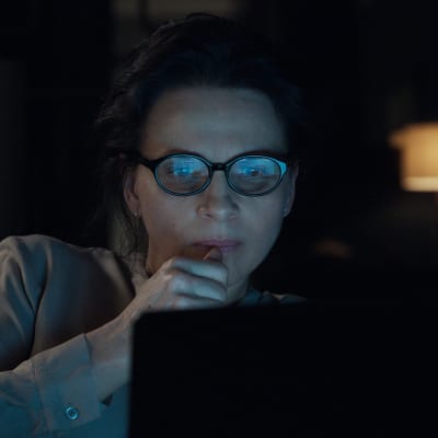 Juliette Binoche som Claire sneglar på sin datorskärm i mörkret.