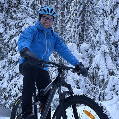 Mies ajaa maastopyörällä lumisessa metsässä.
