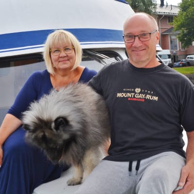 En kvinna, en man och en hund sitter utanpå en blåvit båt i Borgå gästhamn.