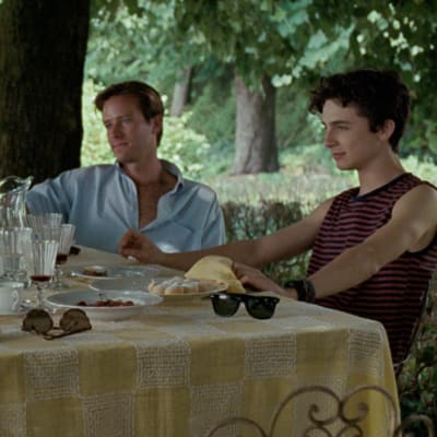 Familjen Perlman och Oliver (Armie Hammer) sitter vid ett bord utomhus, under ett träd och äter.