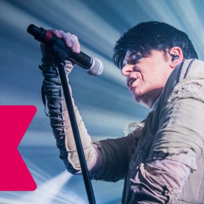 Gary Numan sjunger och håller i en mikrofon som är i en mikrofonställning.