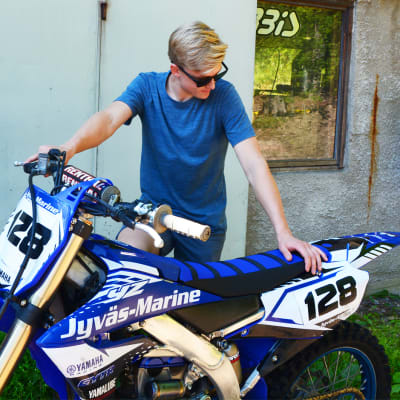 En ung man håller i en blå motorcykel.