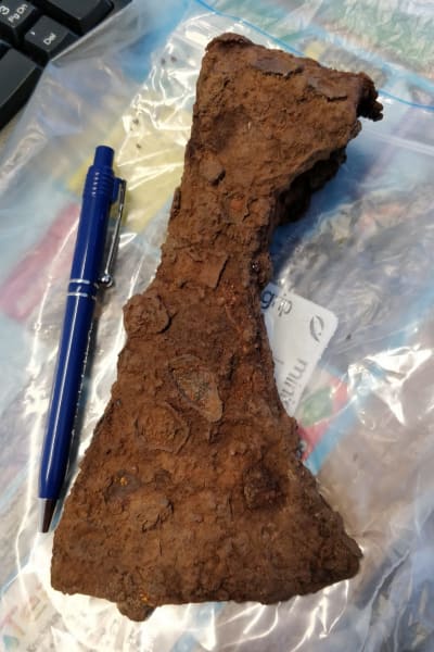 En rostig, 700 år gammal yxa, ligger på en plastpåse. Bredvid ligger en bläckpenna för att visa yxans storlek.