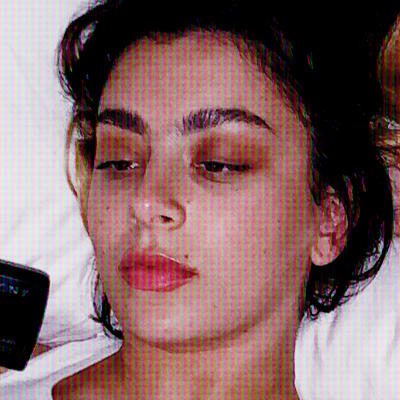 Artisten Charli XCX ligger på sängen med en kamera i handen