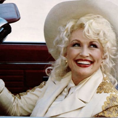 Dolly Parton i cowboyhatt sitter i öppen bil
