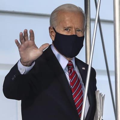 Gråhårig man i kostym och munskydd vinkar åt kameran. President Joe Biden utanför Vita huset den 5 februari 2021, på väg till Wilmington i Delaware.