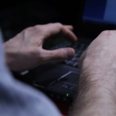 Två händer som skriver på en bärbär dator i halvmörker. 