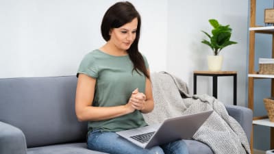 Kvinna som sitter i en soffan med en laptop i famnen.