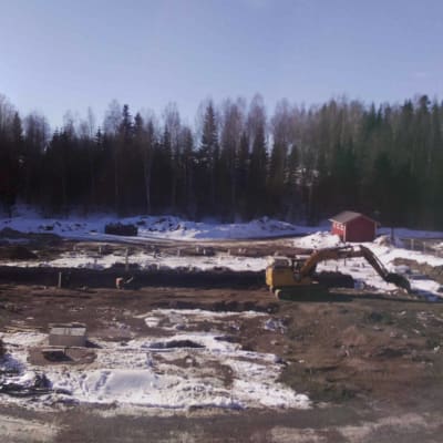 Osin sula ja osin luminen rakennustyömaa, jolla seisoo keltainen kaivinkone. 