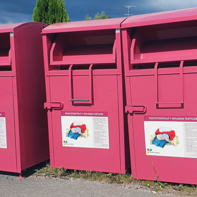 Tre insamlingskärl i rosa färg står bredvid varandra. Man sätter avlagda textilier i dem.