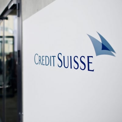 Skylt där det står "Credit Suisse" i bildens vänstermiljö ser man personer gå in samma byggnad som har skylten. 