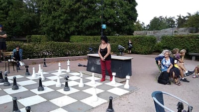 En äldre kvinna spelar schack med stora pjäser i en park. 