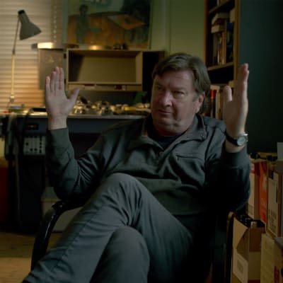 Regissören Aki Kaurismäki sitter i en stol och håller upp händerna för att visa ett mått.