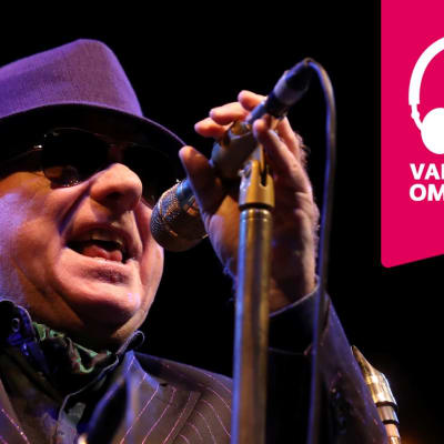 Van Morrison bär hatt och solglasögon och sjunger i en mikrofon som är i en mikrofonställning.
