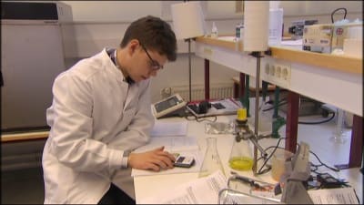 En ung man i vit laboratorierock sitter med räknemaskin.