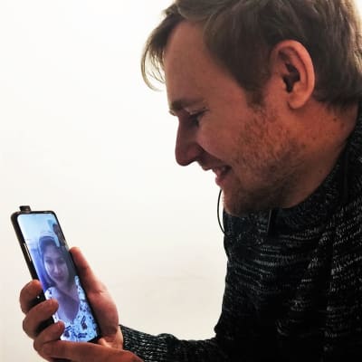 En man ser ner på sin mobilskärm och ler. På skärmen ler en kvinna tillbaka. 