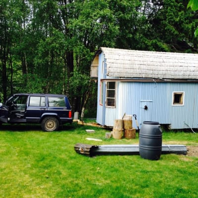ett blåmålat hus som byggts direkt på botten av en gammal husvagn, sommar