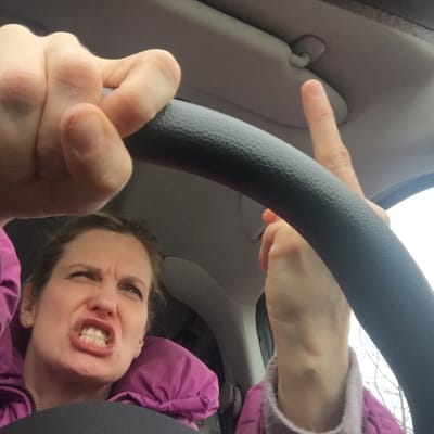 Nainen ratin takana näyttää keskisormea.