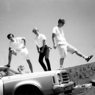 Kolme nuorta miestä valkoisissa t-paidoissa seisovat valkoisen amerikanraudan katolla joutomaa-alueella.