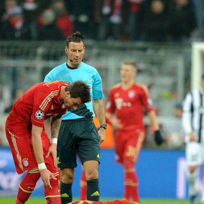 Bayern Münchenin Toni Kroos makaa loukkaantuneena nurmen pinnassa. Mario Mandzukic ja erotuomari Mark Clattenburg seuraavat vierestä.