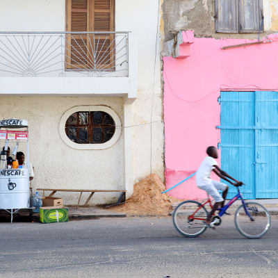 Kuvassa on siirtomaa-aikaisia taloja, hedelmäkioski ja pyöräilijä Saint-Louis'ssa, Senegalissa.