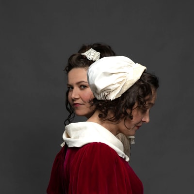 Julia Korander och Nina Hukkinen i fotosession i 1700-talsdräkter. Julia tittar mot kameran, Nina tittar bort.