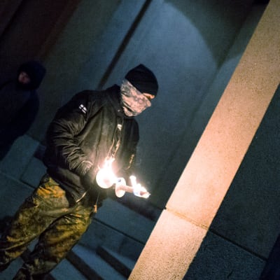 En man som är medlem i Nordiska motståndsrörelsen står med två brinnande facklor i handen i samband med 612-fackeltåget.