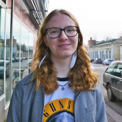 En ung kvinna står på en gata i Lovisa. Hon tittar in i kameran och ler. Bakom henne syns bilar och hus.