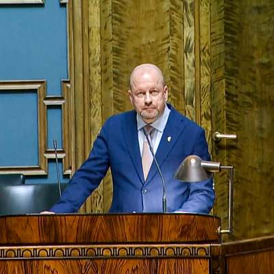 Riksdagledamot Timo Vornanen tittar in i kameran, stående i risdagens talarbås.