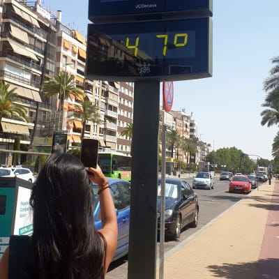 En kvinna tar en bild på en skylt som informerar om att det är 47 grader varmt ute. 