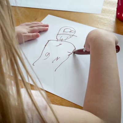 Pieni lapsi piirtää tussilla paperiin isän kuvaa.