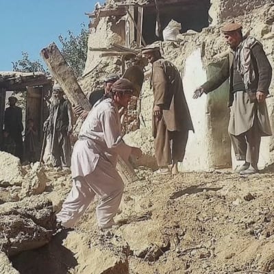Män som står bland husspillror efter jordbävning i Afghanistan.  