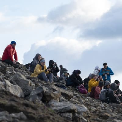 Ihmisiä istuu vuorella katsomassa tulivuoren purkausta.