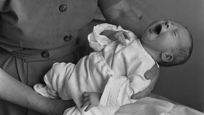 Itkevä vauva kätilön sylissä (1960-luku).