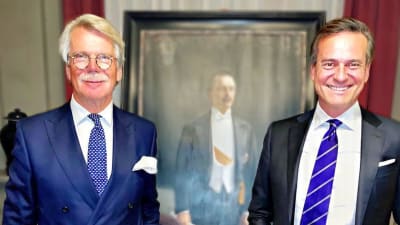 Björn Wahlroos och Mika Ihamuotila står framför en oljemålning. Båda ler rakt in i kameran.