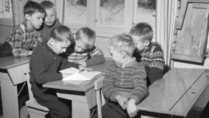 Kansakoulun oppilaita 1950-luvulla. Pojat istuvat pulpeteissa, luokkatoverit katselevat yhden pojan saamaa kirjettä.