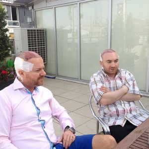 John och Rafi sitter ute på hotellets terrass John och Rafi sitter ute på hotellets terrass efter operationen, med plåster och bandage bak på huvudet