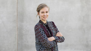 Mia-Maja Wägar har koll på ekonomin. En kvinna med blont uppsatt hår och en blommig blus står framför en grå betongvägg. Hon håller armarna i kors.