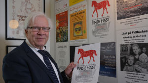 Bo Kronqvist har varit med och utformat årets program för Svenska dagen i Nykarleby under många år. Man med teateraffisch i handen i teaterfoajé i Nykarleby.