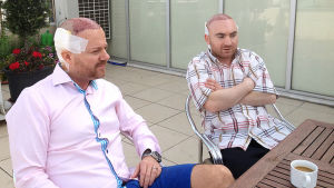 John och Rafi sitter ute på hotellets terrass John och Rafi sitter ute på hotellets terrass efter operationen, med plåster och bandage bak på huvudet
