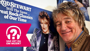 Rod Stewart. Rod Stewart ler framför en plansch av sig själv.