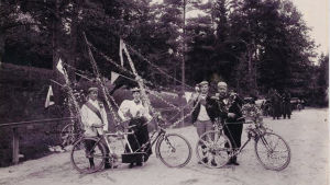 Kukkasin ja viirein koristeltuja polkupyöriä. Arvid Lind lienee mies vasemmalla. Kukkasin ja viirein koristeltuja polkupyöriä. Polkupyöräilijöitä 1900-luvun alussa.