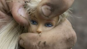 Våldet och oron i karaktären Brunos vardag sätter nästan inga spår i karaktären, enligt recensenten Adrian Perera. Smutsig hand klämmer Barbie-docka.