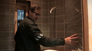 Juha-Pekka iloitsee wc:n upean laatoituksen valmistumisesta. Mies koskettelee vastarakennetun talon seinää