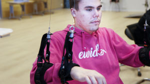 Elias pelaa kuntouttavaa peliä. Hänen käsissään on pelaamista helpottavat käsituet.