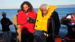 Nicolas Miguiz från Proactiva Open Arms hjälper en äldre man med skidat ben upp på stranden. Miguiz Nicolas från Proactiva Open Arms hjälper en äldre man med skidat ben upp på stranden.