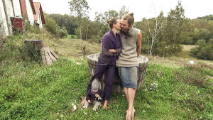 Frida och Mikkel framför den trätunna som hon fött alla sina barn i. Frida och Mikkel står lutade mot ett spann på bakgården.
