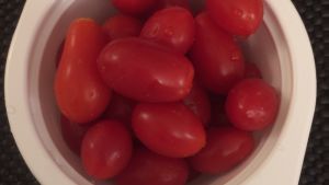 Minitomaatteja pestyssä valkoisessa muovisessa mikroateriakupissa, mustalla kumialustalla
