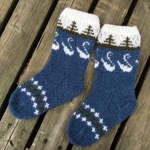 Stickade sockor med svanar och granar. Stickade sockor i blått med vita svanar och gröna granar.